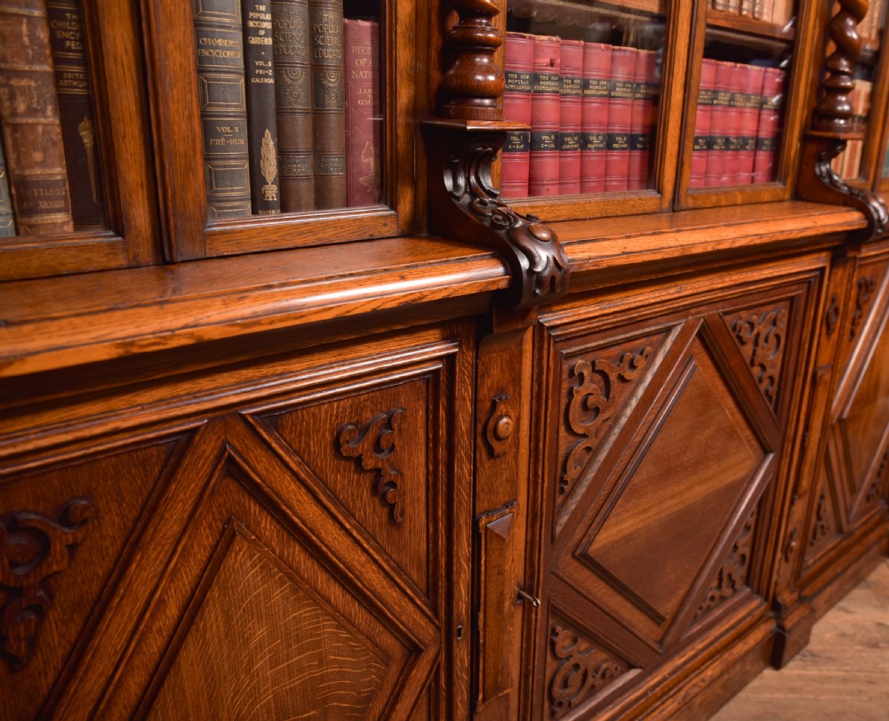 A large Victorian oak bookcase featuring glazed upper doors flanked by barley twist columns with turned finials above carved diamond panel doors. View XX