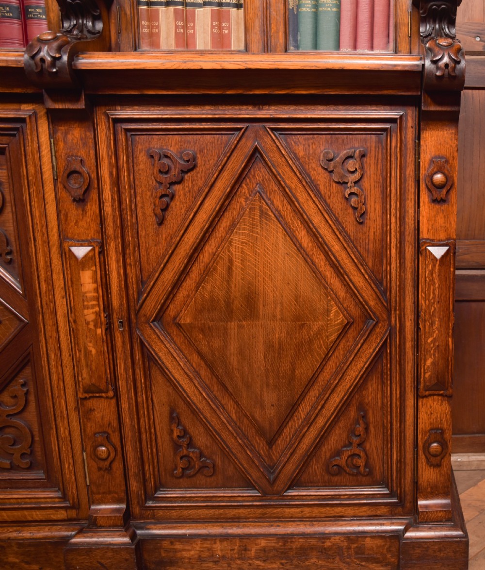 A large Victorian oak bookcase featuring glazed upper doors flanked by barley twist columns with turned finials above carved diamond panel doors. View XXIV