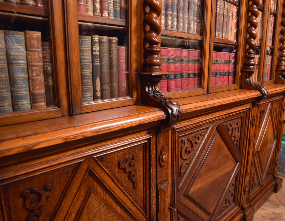 A large Victorian oak bookcase featuring glazed upper doors flanked by barley twist columns with turned finials above carved diamond panel doors. View XXVI