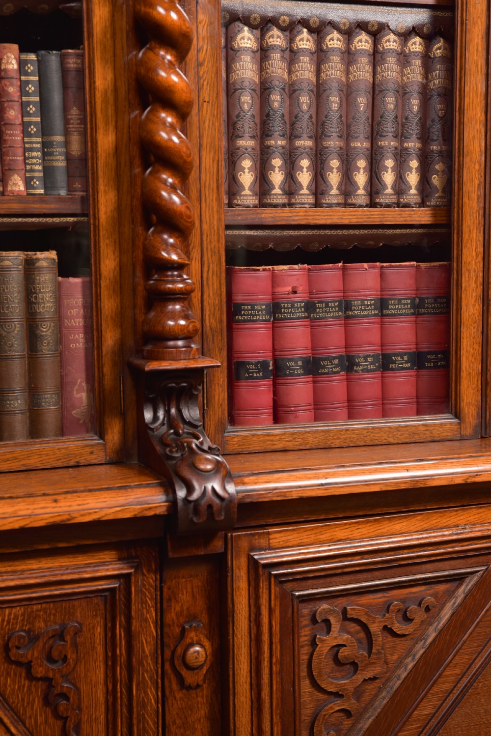A large Victorian oak bookcase featuring glazed upper doors flanked by barley twist columns with turned finials above carved diamond panel doors. View XXX