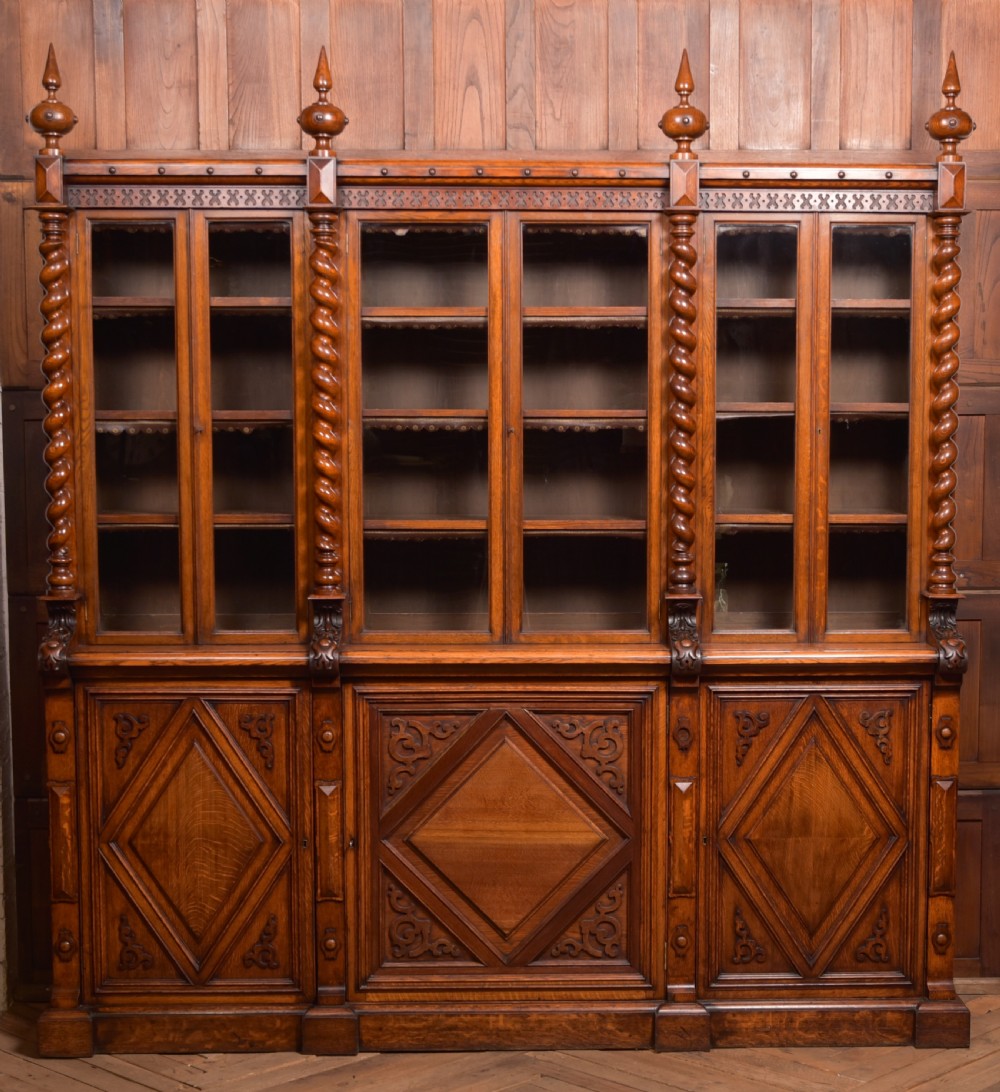 A large Victorian oak bookcase featuring glazed upper doors flanked by barley twist columns with turned finials above carved diamond panel doors. View XXXI