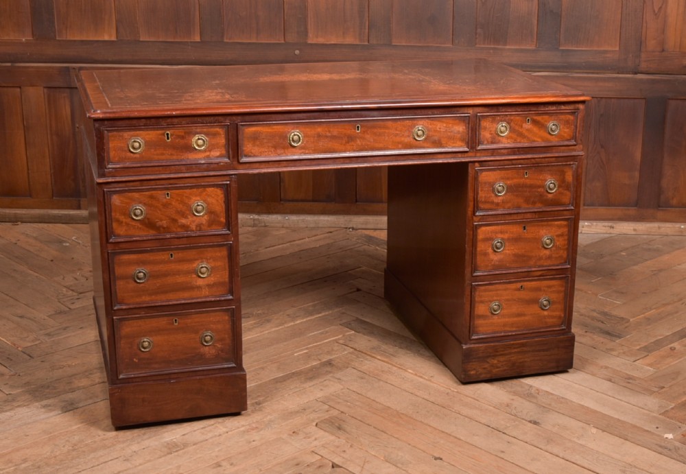 An Edwardian mahogany pedestal desk with nine drawers, brass ring handles, and a leather-inset writing surface.