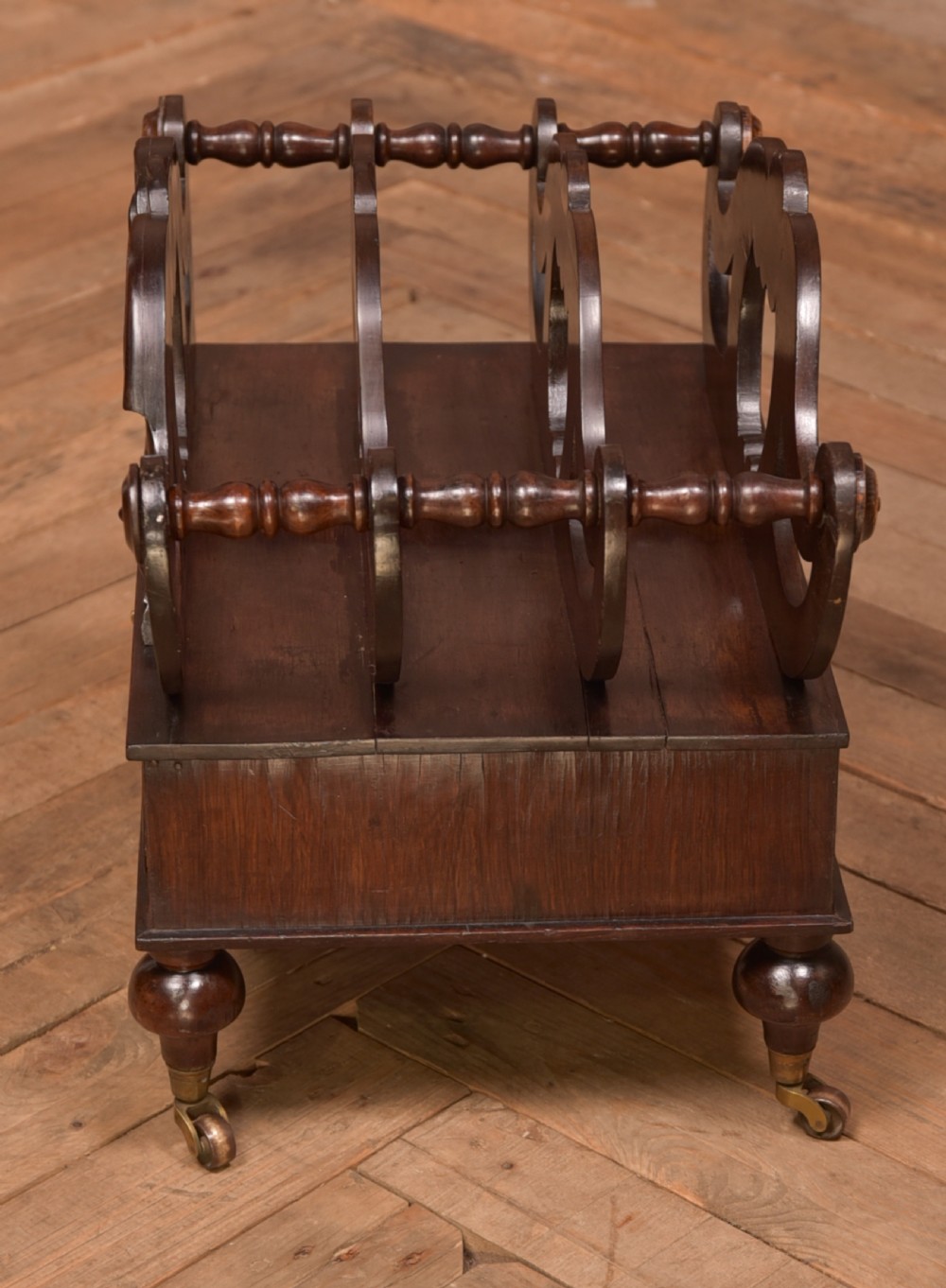 A Victorian rosewood Canterbury featuring four carved scroll dividers above a single base drawer, supported by turned legs on brass castors. View III