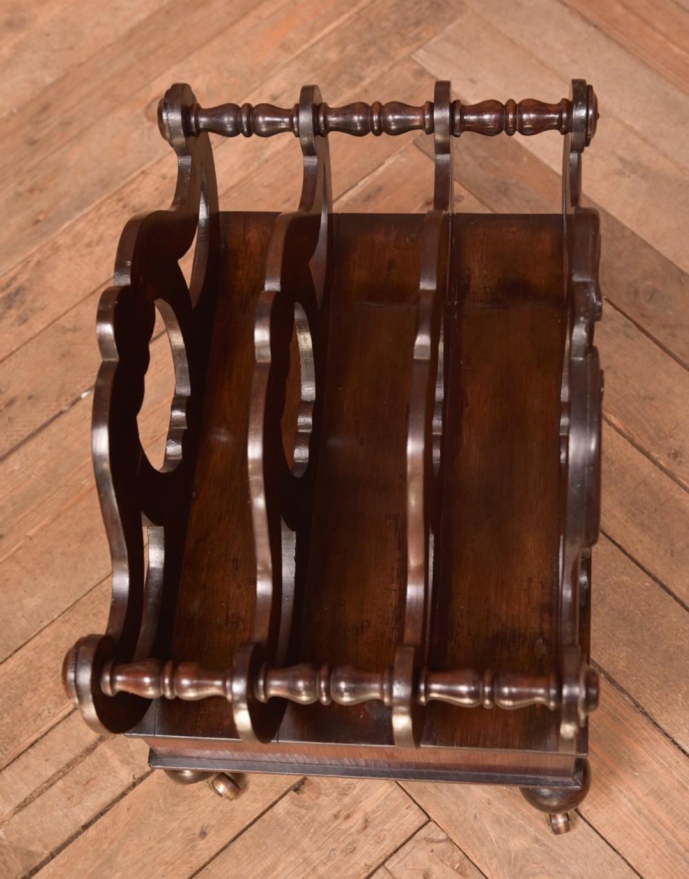 A Victorian rosewood Canterbury featuring four carved scroll dividers above a single base drawer, supported by turned legs on brass castors. View VIII