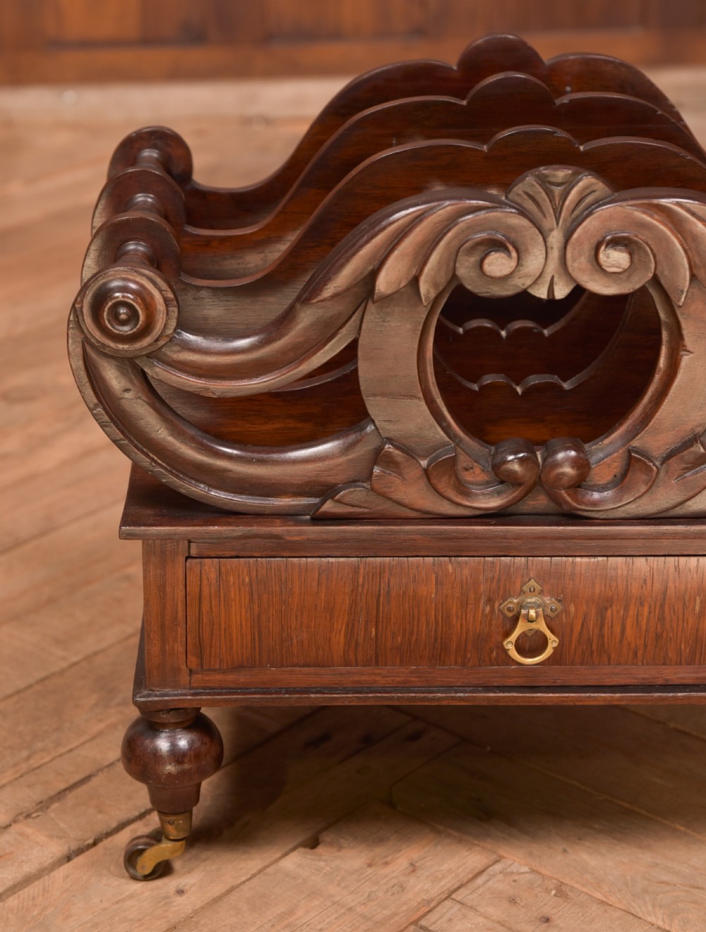 A Victorian rosewood Canterbury featuring four carved scroll dividers above a single base drawer, supported by turned legs on brass castors. View IX