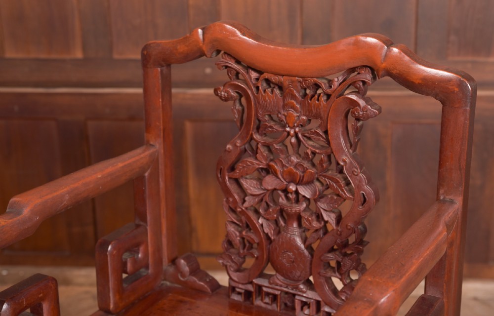 A carved reddish-brown lacquered wooden Chinese armchair featuring an intricate floral splat back, stepped armrests, and decorative carved apron. View II