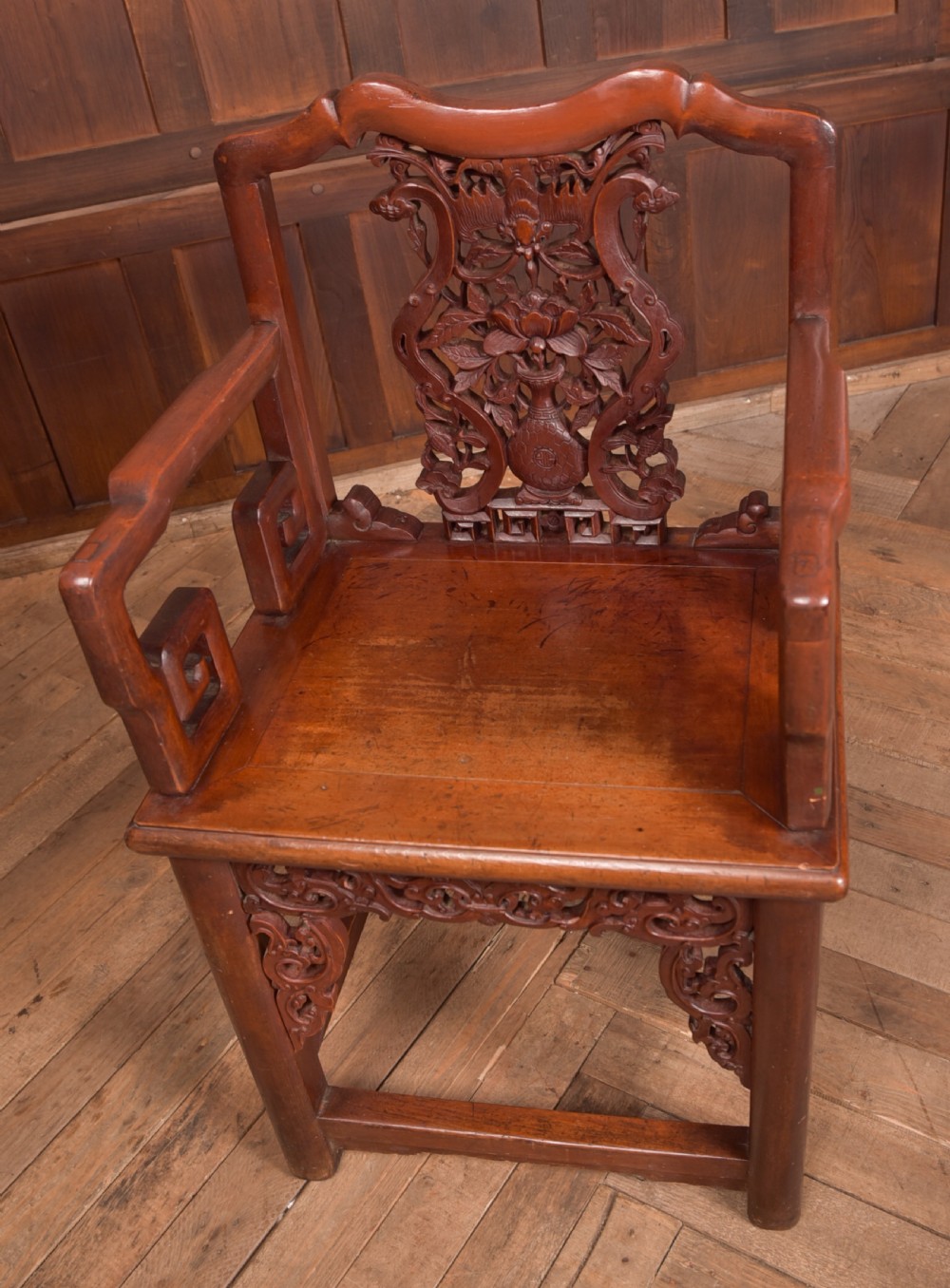 A carved reddish-brown lacquered wooden Chinese armchair featuring an intricate floral splat back, stepped armrests, and decorative carved apron. View III