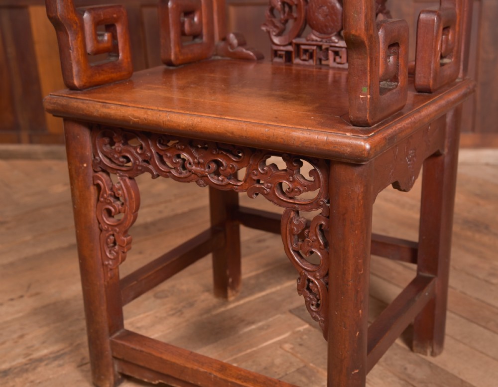A carved reddish-brown lacquered wooden Chinese armchair featuring an intricate floral splat back, stepped armrests, and decorative carved apron. View IV