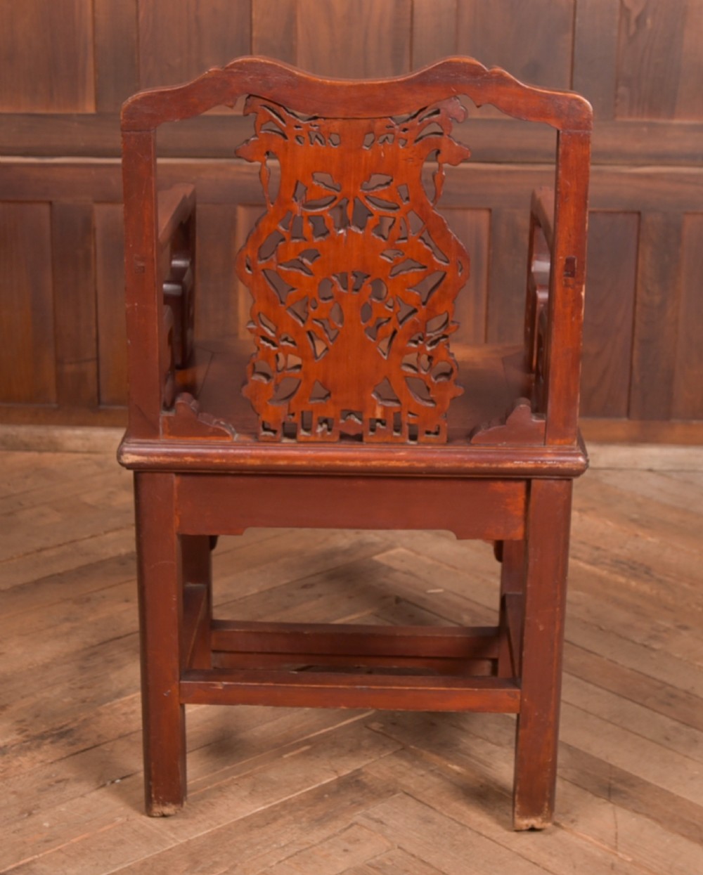 A carved reddish-brown lacquered wooden Chinese armchair featuring an intricate floral splat back, stepped armrests, and decorative carved apron. View VI