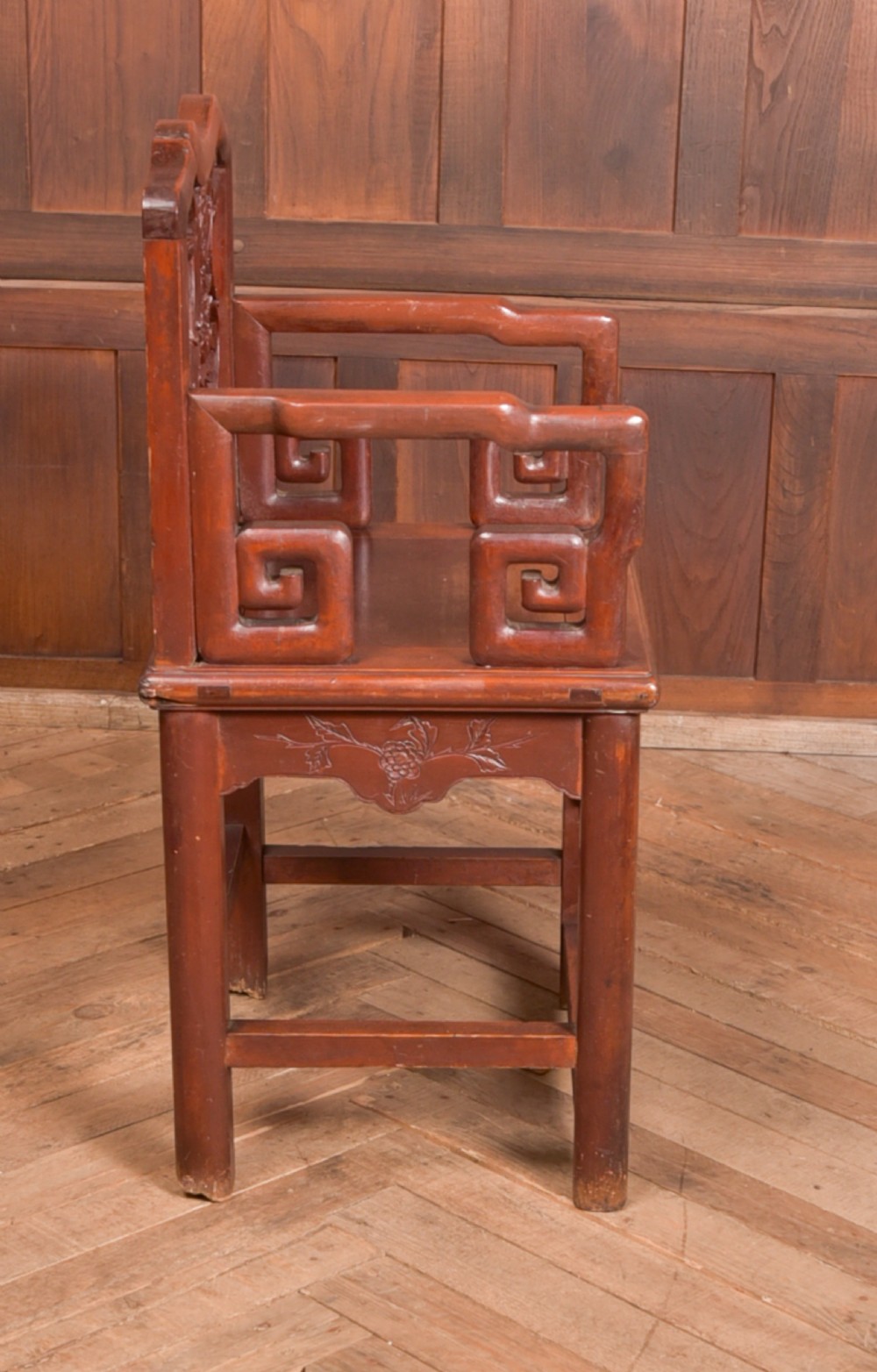 A carved reddish-brown lacquered wooden Chinese armchair featuring an intricate floral splat back, stepped armrests, and decorative carved apron. View VII
