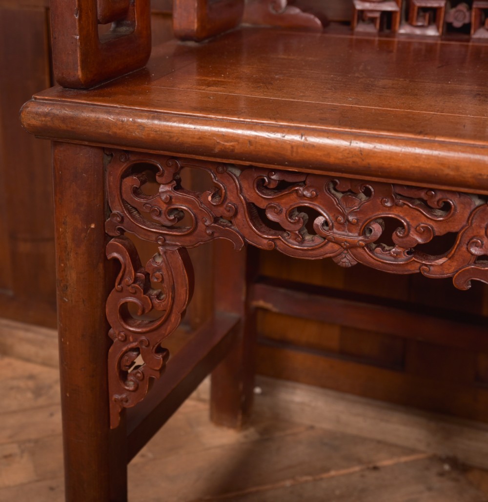 A carved reddish-brown lacquered wooden Chinese armchair featuring an intricate floral splat back, stepped armrests, and decorative carved apron. View IX