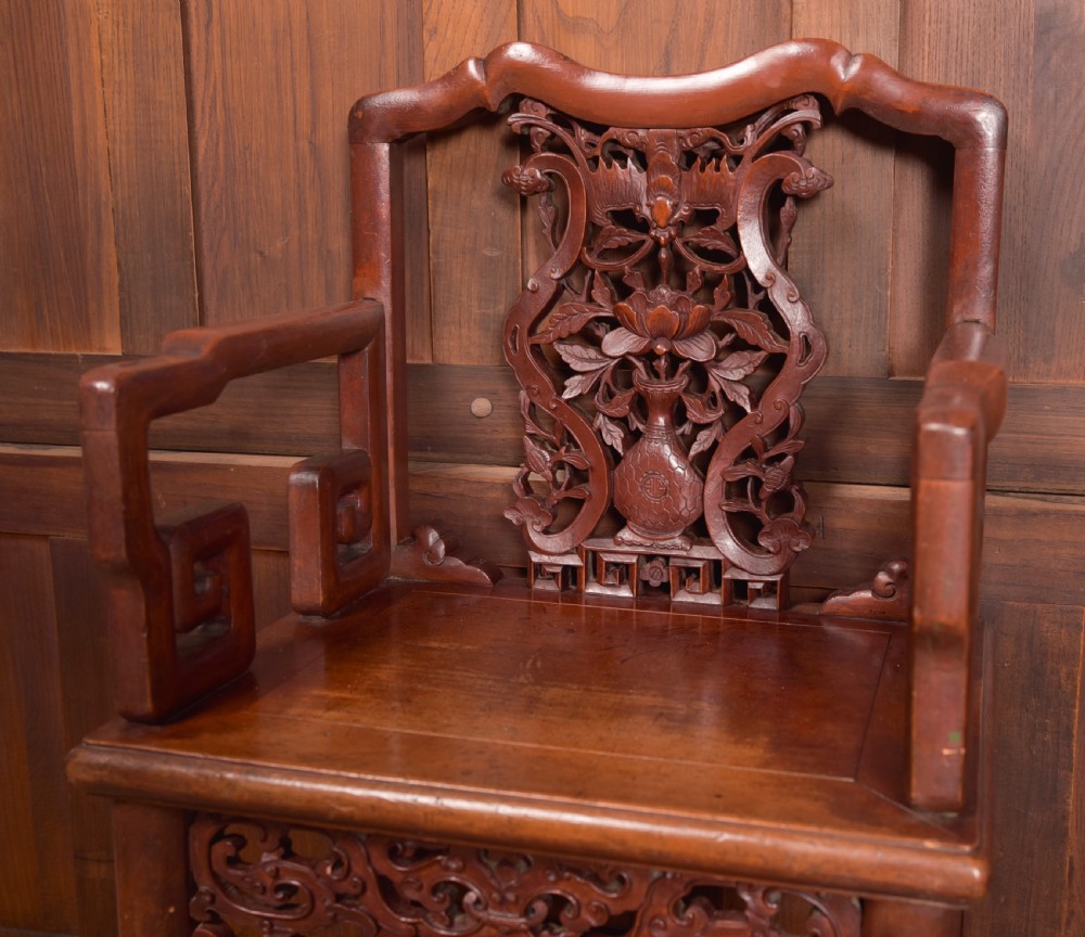 A carved reddish-brown lacquered wooden Chinese armchair featuring an intricate floral splat back, stepped armrests, and decorative carved apron. View X
