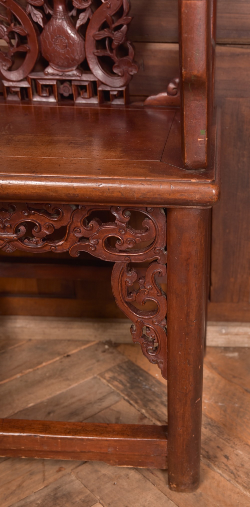 A carved reddish-brown lacquered wooden Chinese armchair featuring an intricate floral splat back, stepped armrests, and decorative carved apron. View XI