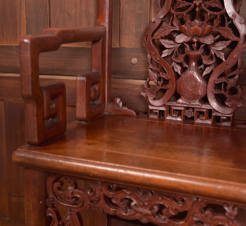 A carved reddish-brown lacquered wooden Chinese armchair featuring an intricate floral splat back, stepped armrests, and decorative carved apron. View XII