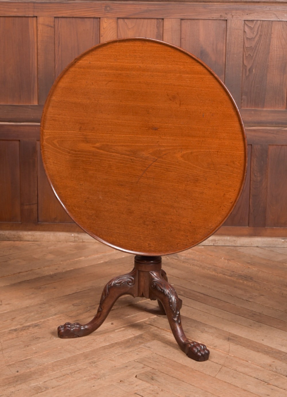 A Georgian mahogany circular snap-top supper table displayed vertically on a turned pedestal stem with carved cabriole legs and ball-and-claw feet.