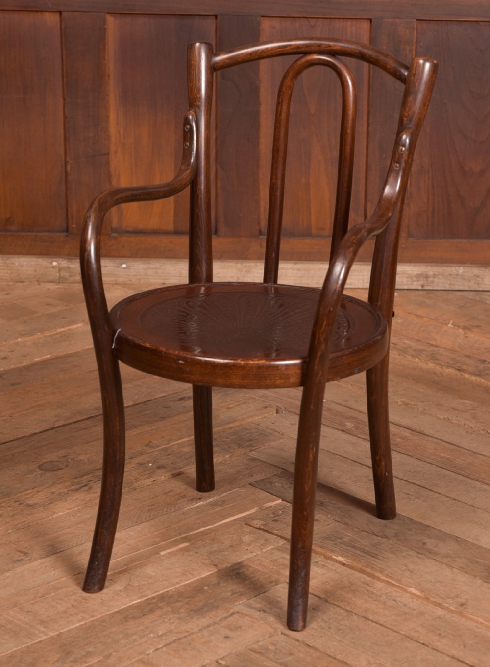 A dark brown childs bentwood armchair featuring a curved backrest, sweeping armrests, and an embossed wooden seat.