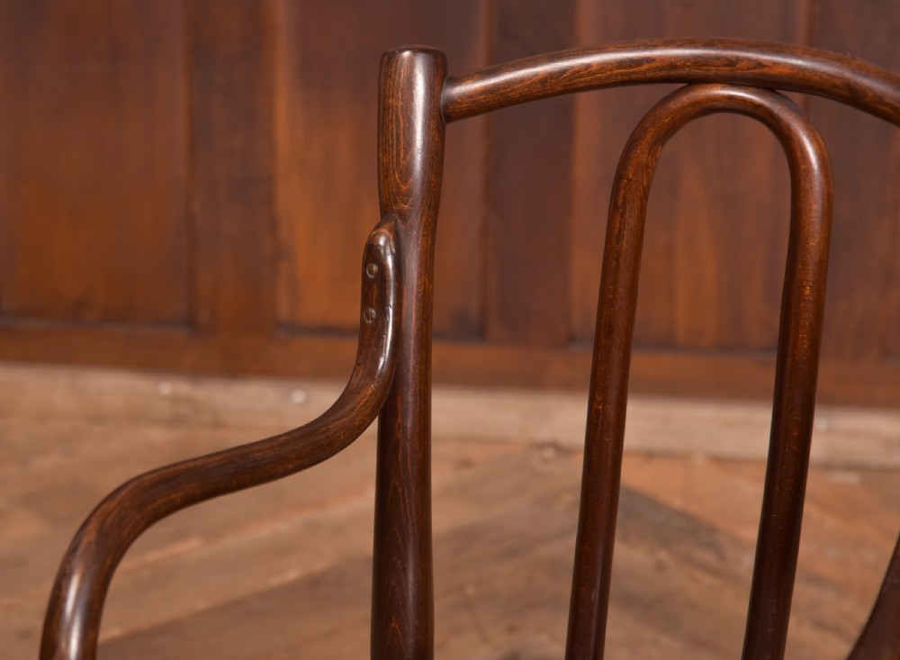 A dark brown childs bentwood armchair featuring a curved backrest, sweeping armrests, and an embossed wooden seat. View II