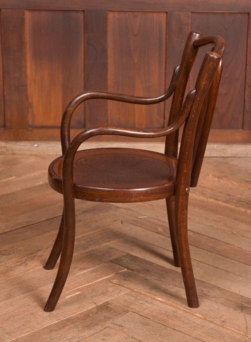 A dark brown childs bentwood armchair featuring a curved backrest, sweeping armrests, and an embossed wooden seat. View III
