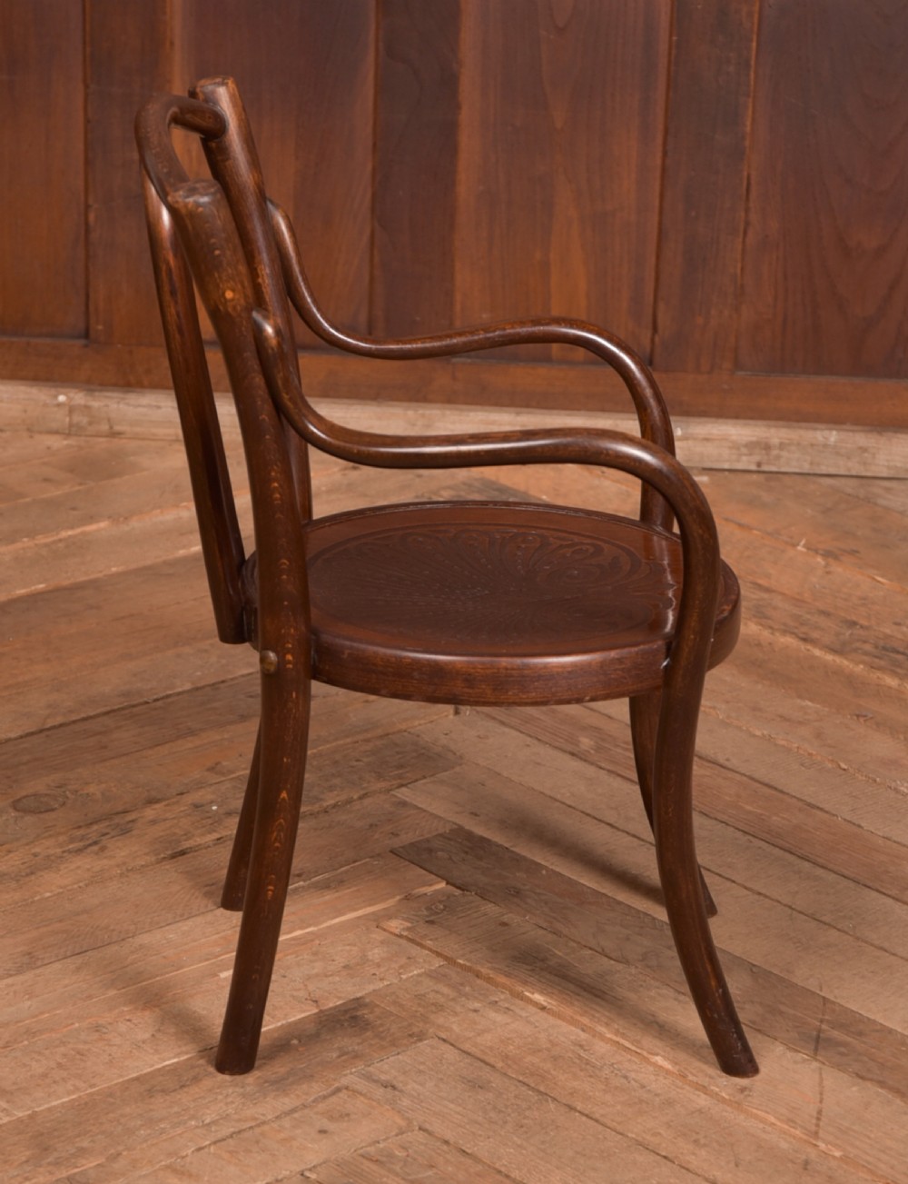 A dark brown childs bentwood armchair featuring a curved backrest, sweeping armrests, and an embossed wooden seat. View IV