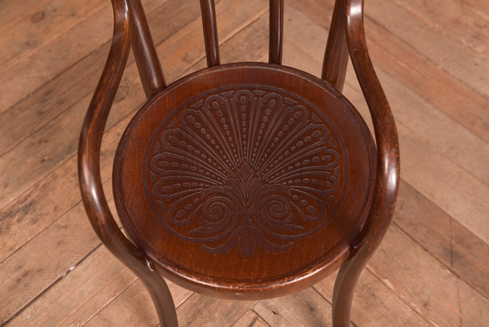 A dark brown childs bentwood armchair featuring a curved backrest, sweeping armrests, and an embossed wooden seat. View V