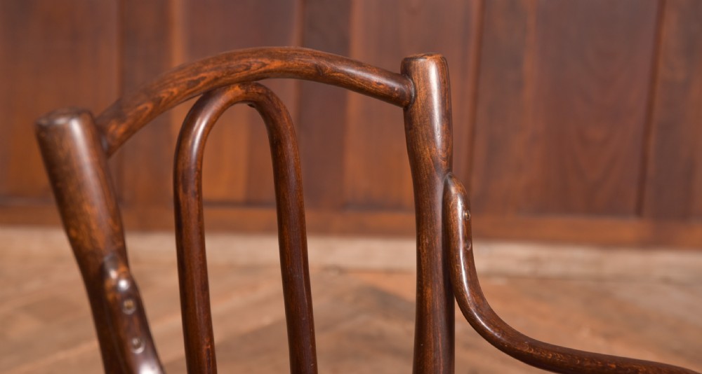 A dark brown childs bentwood armchair featuring a curved backrest, sweeping armrests, and an embossed wooden seat. View IX