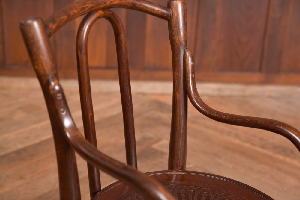 A dark brown childs bentwood armchair featuring a curved backrest, sweeping armrests, and an embossed wooden seat. View X