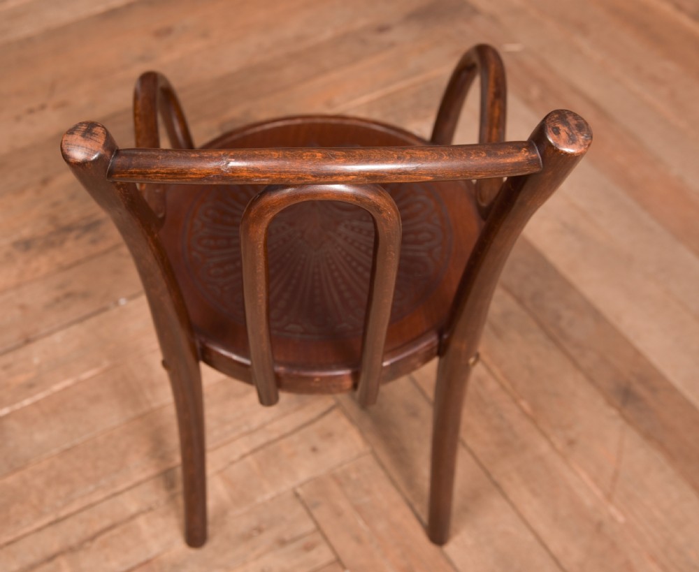 A dark brown childs bentwood armchair featuring a curved backrest, sweeping armrests, and an embossed wooden seat. View XII
