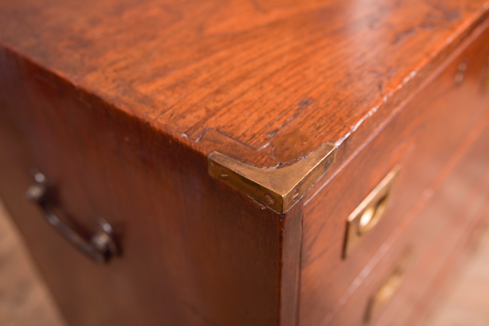 A nineteenth-century teak military campaign chest of drawers with flush brass handles, corner brackets, and turned feet. View V