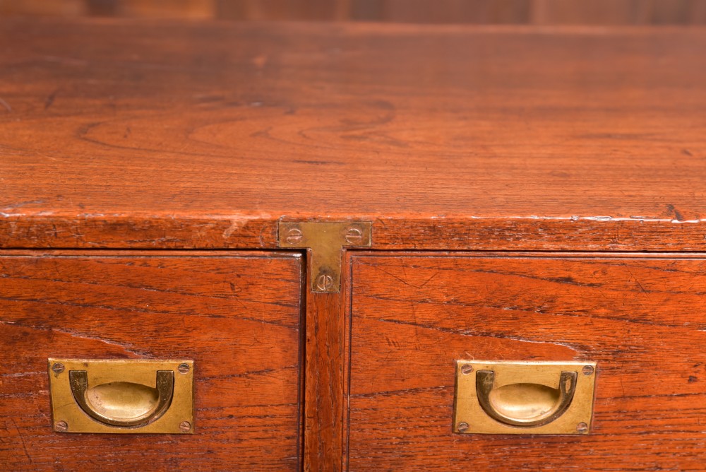 A nineteenth-century teak military campaign chest of drawers with flush brass handles, corner brackets, and turned feet. View XI