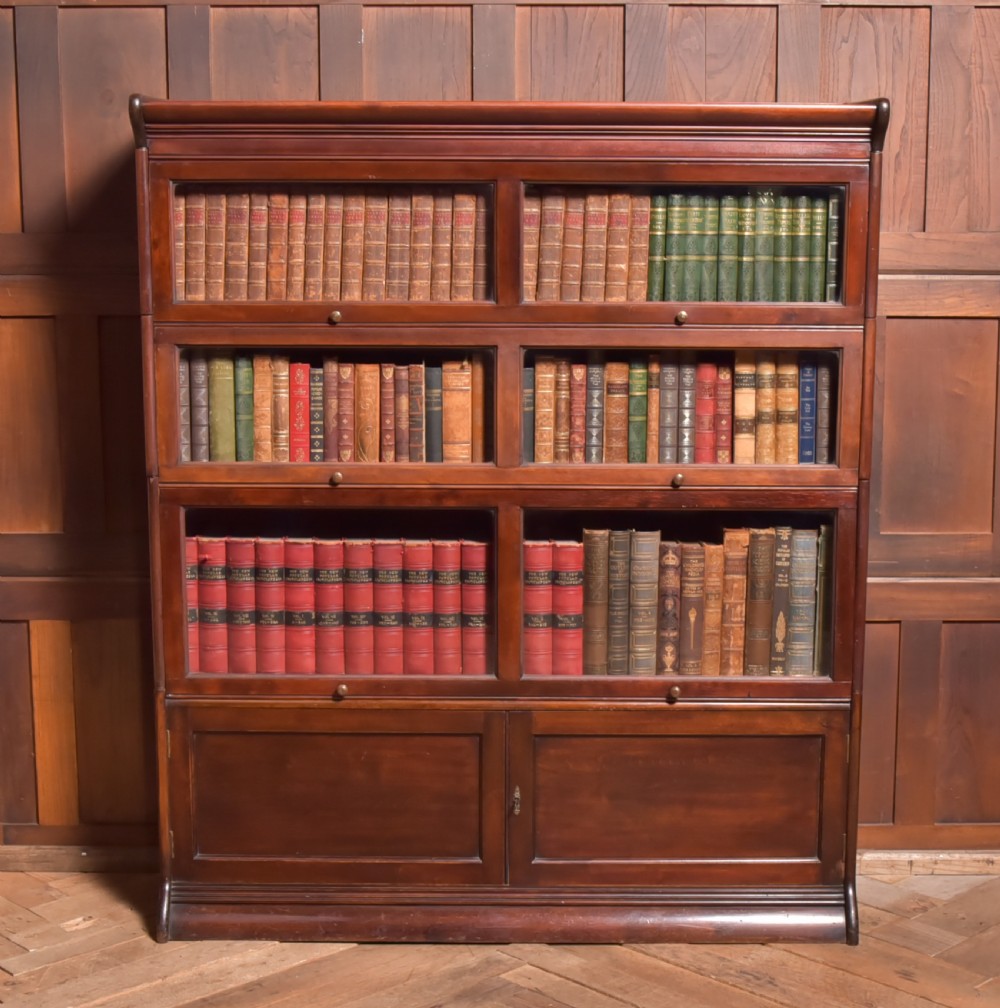 A large double-width mahogany sectional bookcase featuring three tiers of glazed lift-up doors filled with antique books above a solid wooden double cupboard base.
