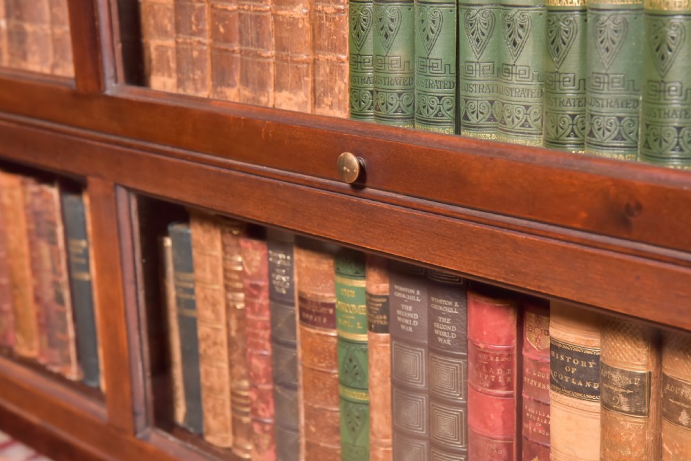 A large double-width mahogany sectional bookcase featuring three tiers of glazed lift-up doors filled with antique books above a solid wooden double cupboard base. View II