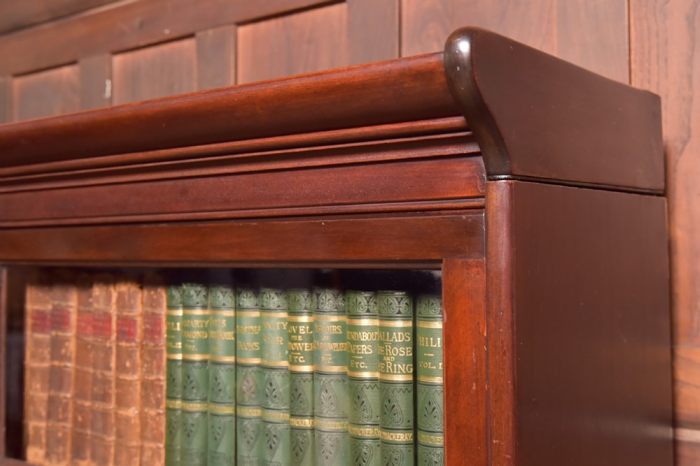 A large double-width mahogany sectional bookcase featuring three tiers of glazed lift-up doors filled with antique books above a solid wooden double cupboard base. View III