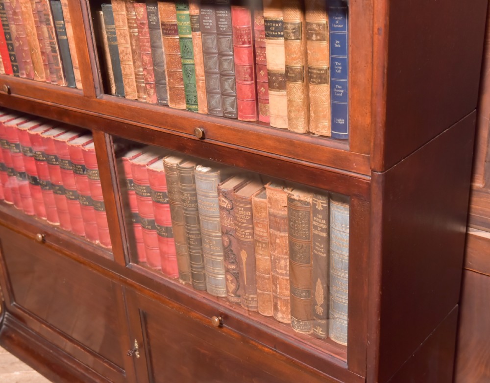 A large double-width mahogany sectional bookcase featuring three tiers of glazed lift-up doors filled with antique books above a solid wooden double cupboard base. View V