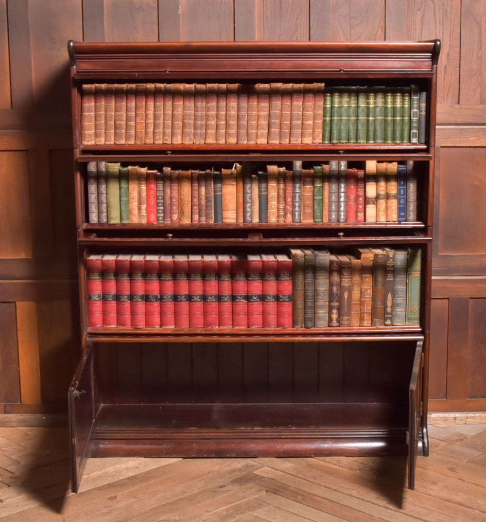 A large double-width mahogany sectional bookcase featuring three tiers of glazed lift-up doors filled with antique books above a solid wooden double cupboard base. View VI