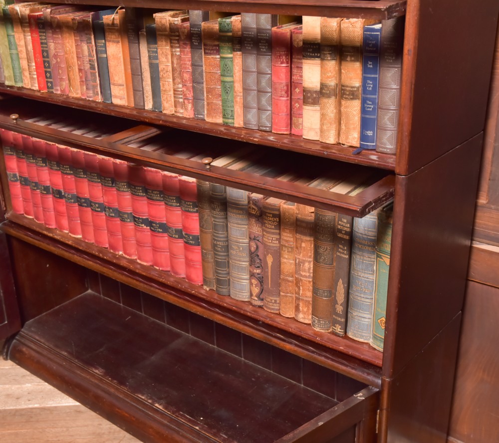 A large double-width mahogany sectional bookcase featuring three tiers of glazed lift-up doors filled with antique books above a solid wooden double cupboard base. View VII
