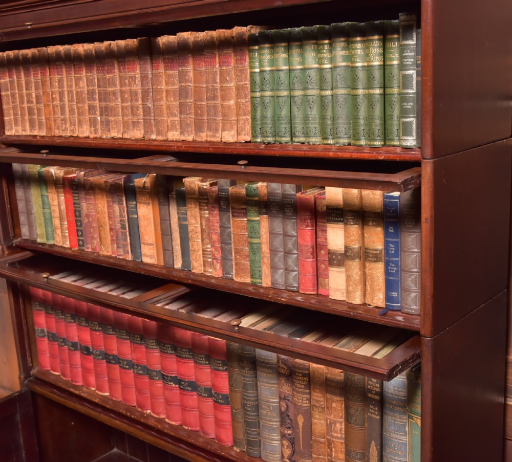 A large double-width mahogany sectional bookcase featuring three tiers of glazed lift-up doors filled with antique books above a solid wooden double cupboard base. View VIII