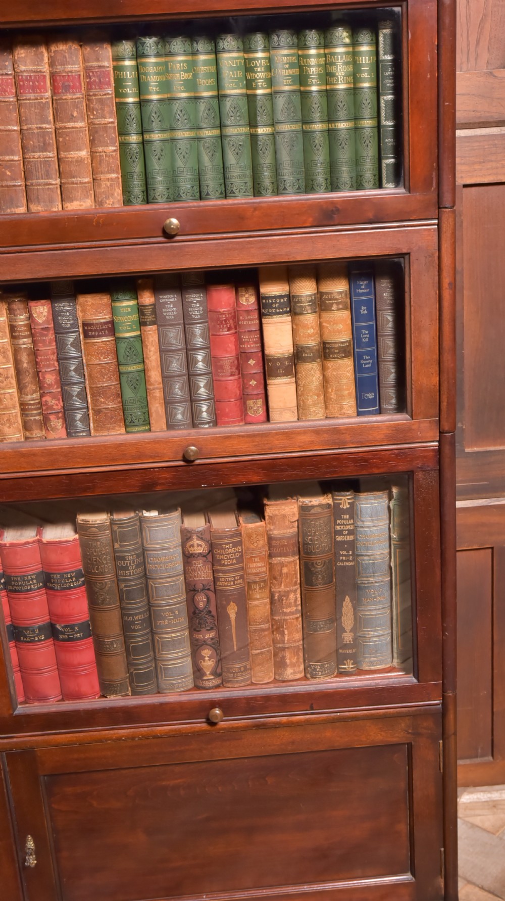 A large double-width mahogany sectional bookcase featuring three tiers of glazed lift-up doors filled with antique books above a solid wooden double cupboard base. View IX