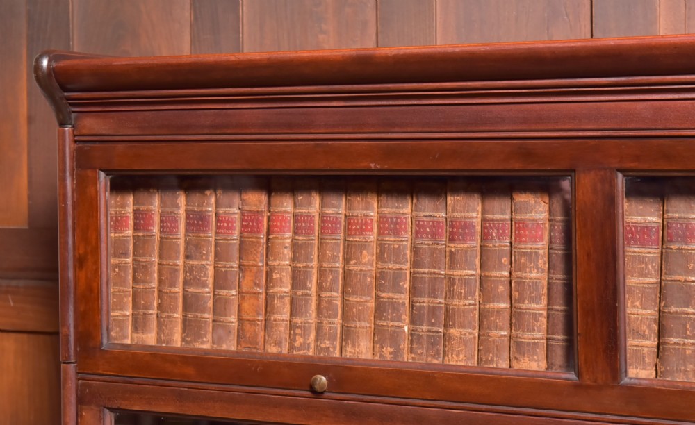 A large double-width mahogany sectional bookcase featuring three tiers of glazed lift-up doors filled with antique books above a solid wooden double cupboard base. View X