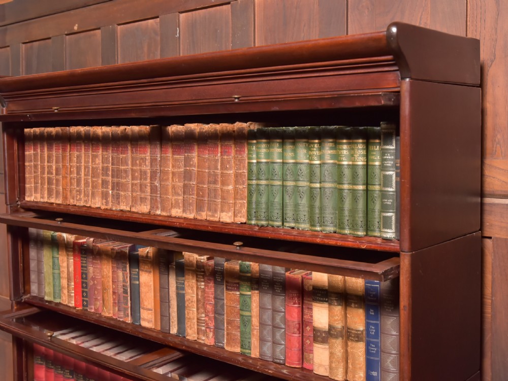 A large double-width mahogany sectional bookcase featuring three tiers of glazed lift-up doors filled with antique books above a solid wooden double cupboard base. View XI