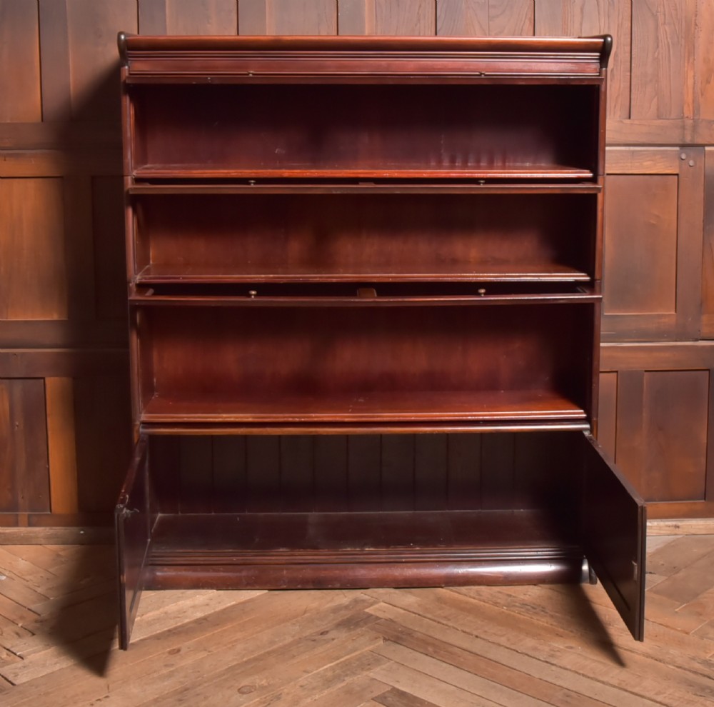 A large double-width mahogany sectional bookcase featuring three tiers of glazed lift-up doors filled with antique books above a solid wooden double cupboard base. View XIII