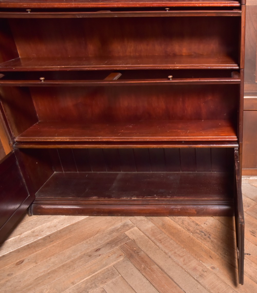 A large double-width mahogany sectional bookcase featuring three tiers of glazed lift-up doors filled with antique books above a solid wooden double cupboard base. View XIX