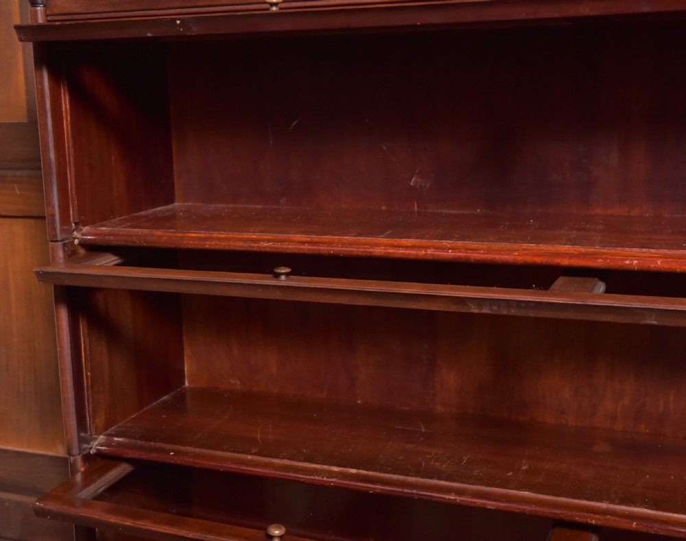 A large double-width mahogany sectional bookcase featuring three tiers of glazed lift-up doors filled with antique books above a solid wooden double cupboard base. View XXI