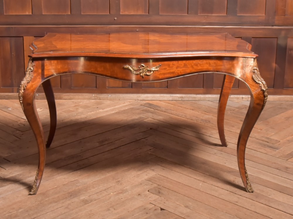 A Victorian walnut centre table featuring a serpentine top, gilt ormolu mounts, and cabriole legs on a parquet floor.