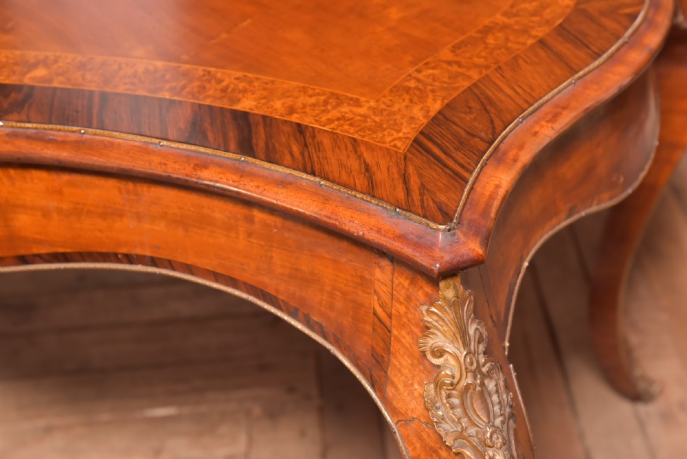 A Victorian walnut centre table featuring a serpentine top, gilt ormolu mounts, and cabriole legs on a parquet floor. View V