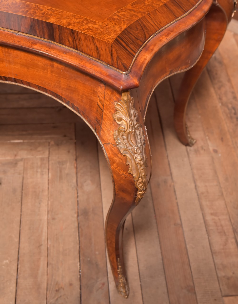 A Victorian walnut centre table featuring a serpentine top, gilt ormolu mounts, and cabriole legs on a parquet floor. View VI