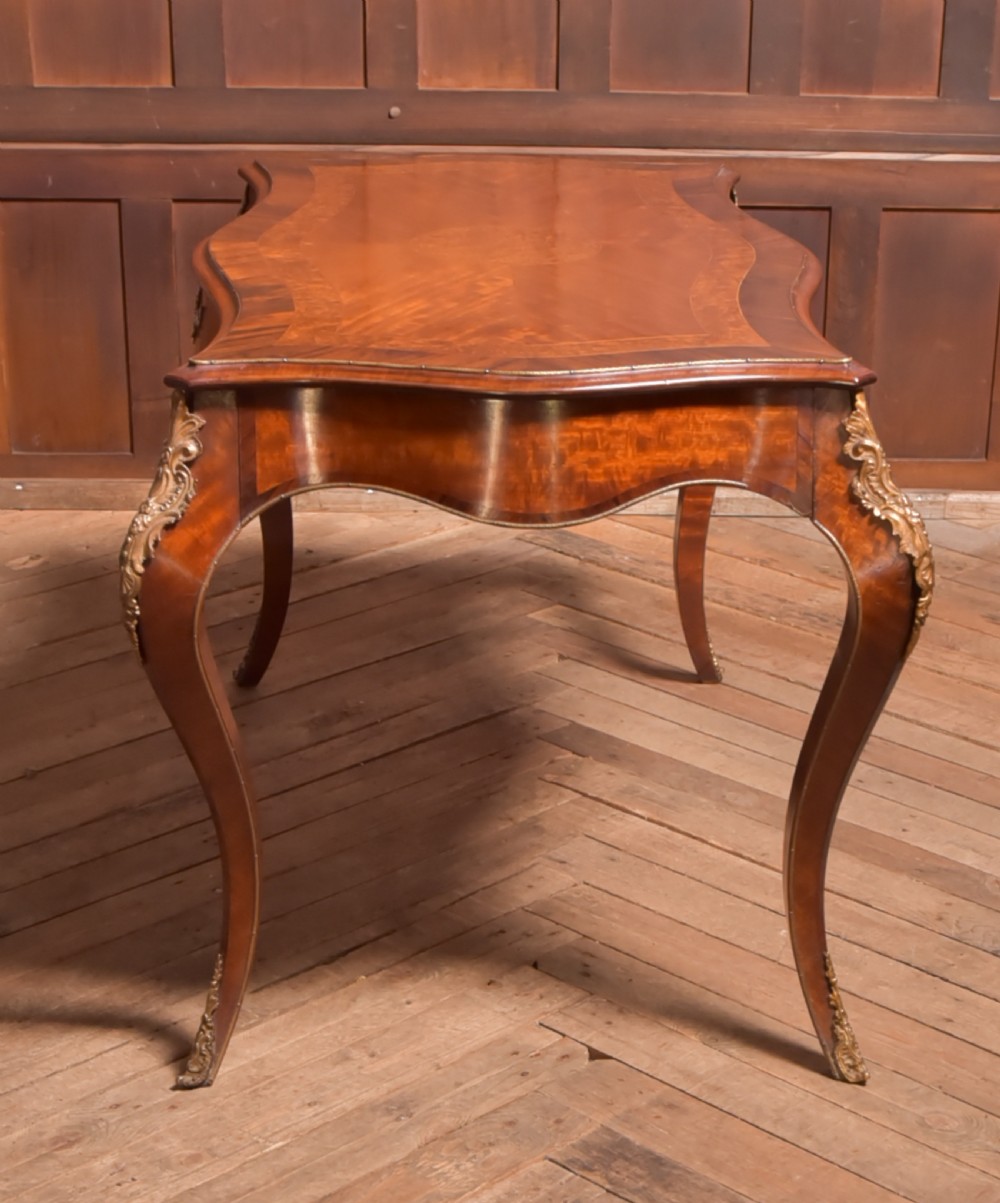 A Victorian walnut centre table featuring a serpentine top, gilt ormolu mounts, and cabriole legs on a parquet floor. View VIII