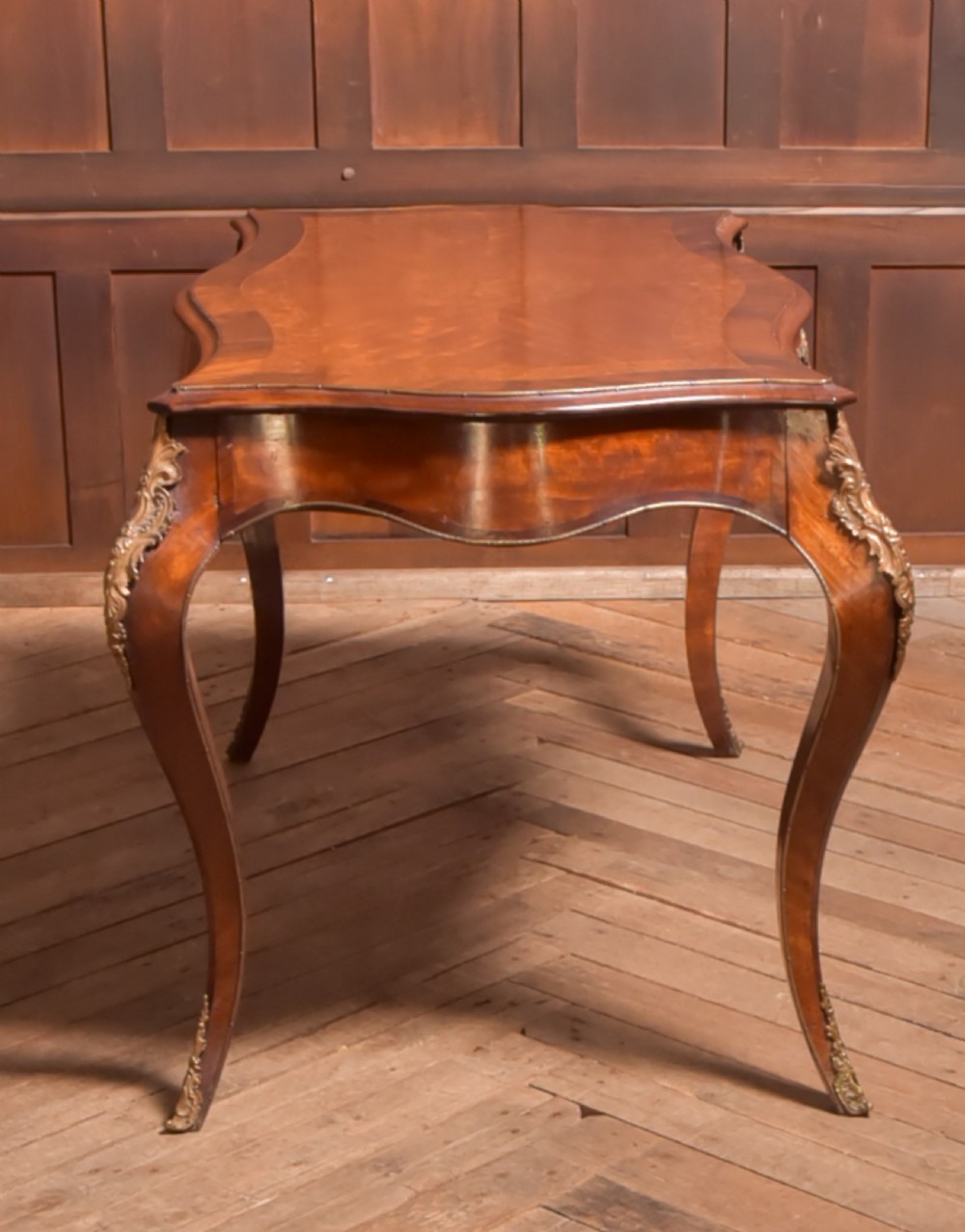 A Victorian walnut centre table featuring a serpentine top, gilt ormolu mounts, and cabriole legs on a parquet floor. View IX
