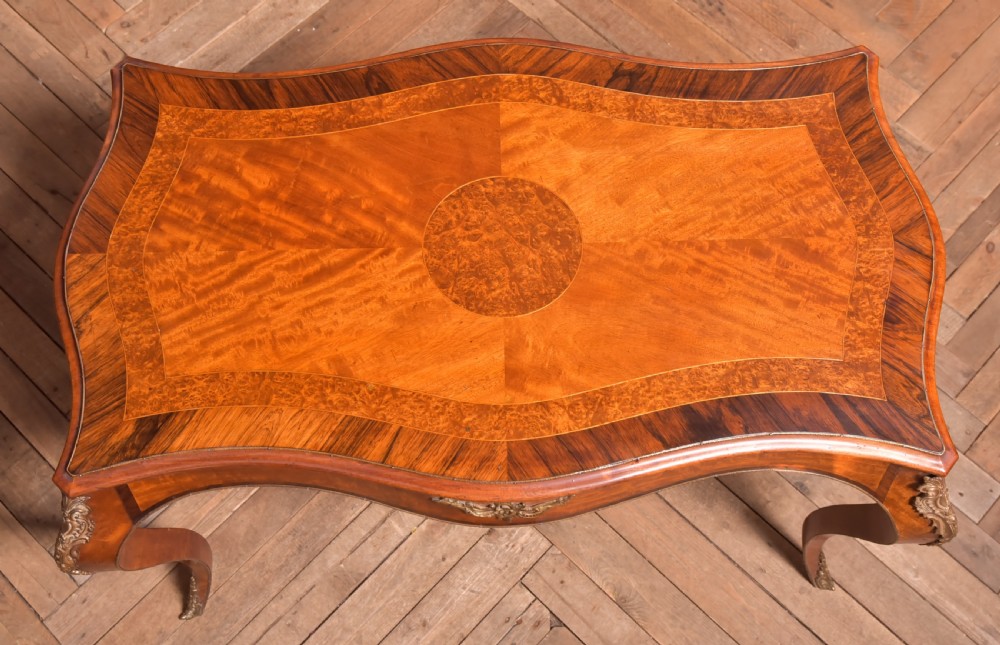 A Victorian walnut centre table featuring a serpentine top, gilt ormolu mounts, and cabriole legs on a parquet floor. View XII