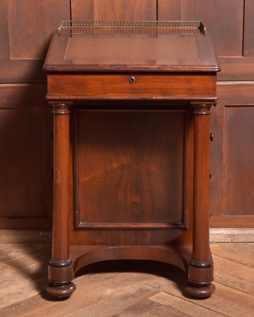 A Victorian rosewood Davenport desk featuring a slanted leather-inset writing surface, brass gallery rail, turned front columns, and side drawers.