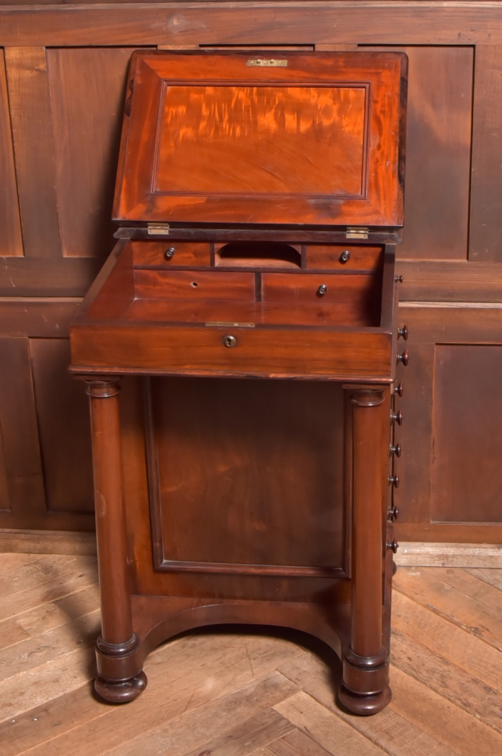 A Victorian rosewood Davenport desk featuring a slanted leather-inset writing surface, brass gallery rail, turned front columns, and side drawers. View V
